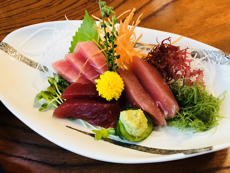 Cuts of tuna sashimi arranged with vegetables and a flower on a serving plate.