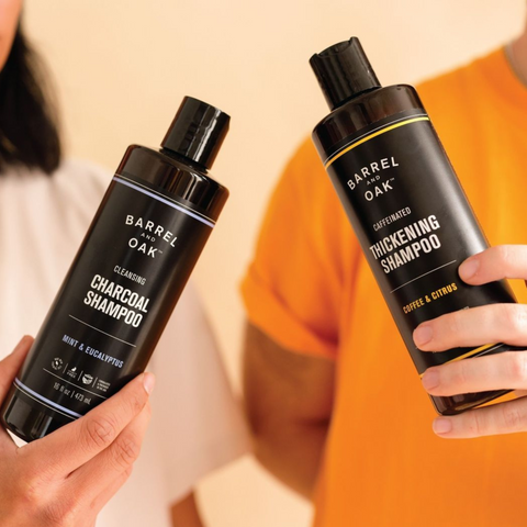 two people holding Barrel & oak shampoo to display bottle size and packaging. labels read: charcoal shampoo for the bottle on the left and thickening shampoo for the bottle on the right