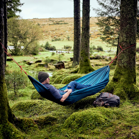 Gentlemen's hardware blue travel hammock in the green woods with a person laying in it