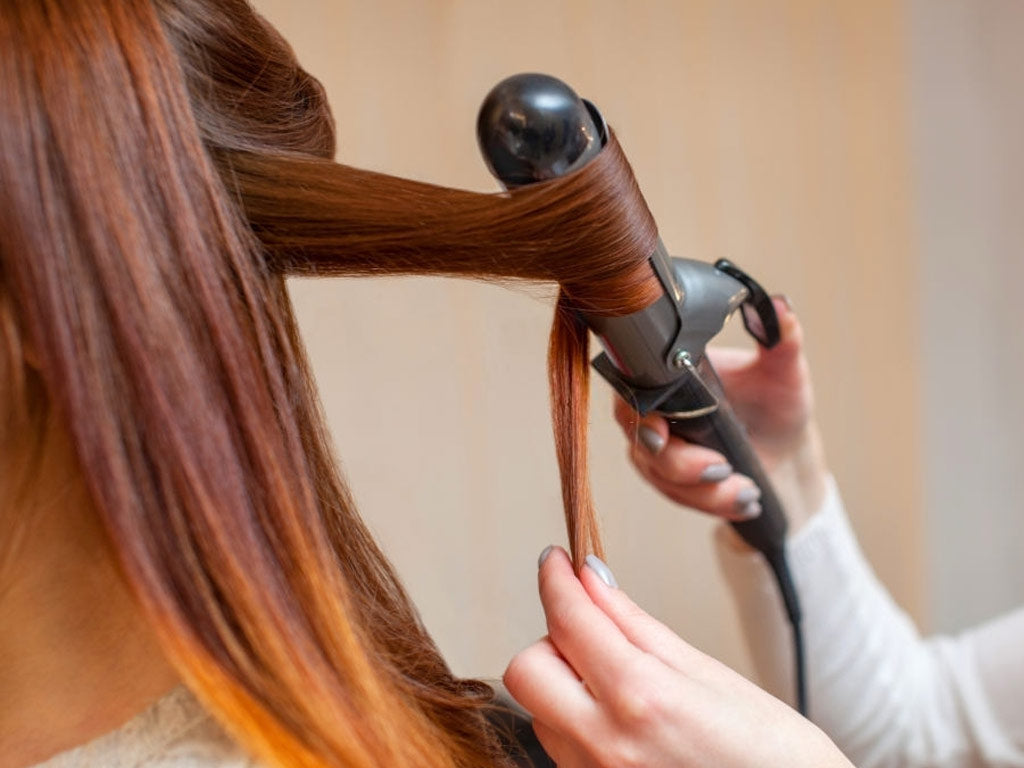 stylist is styling her client hair with iron tool