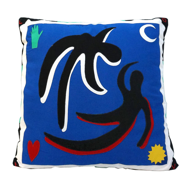 Cushion with a dark blue background and white and black border. The design shows two figures floating - with black, white and red fabric. In the top left corner is a green hand, bottom left a red heart, top right a white crescent moon and bottom right a yellow star.  | © Pangea 2024