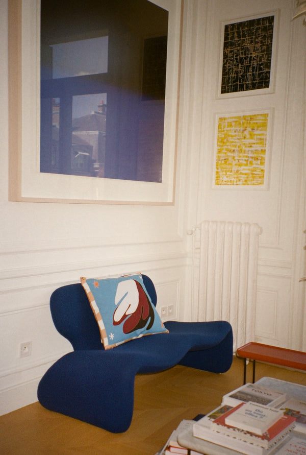 The cushion is displayed in a home, on a dark blue sofa. | © Pangea 2024