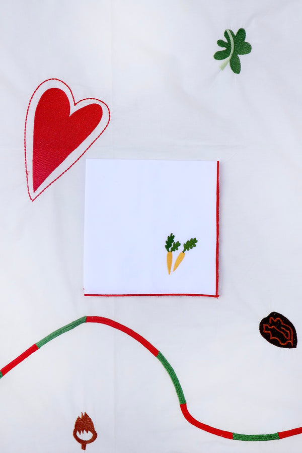 This napkin has two light orange carrots with green stalks embroidered. | © Pangea 2024