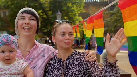 Two women hold their baby at a Pride parade.