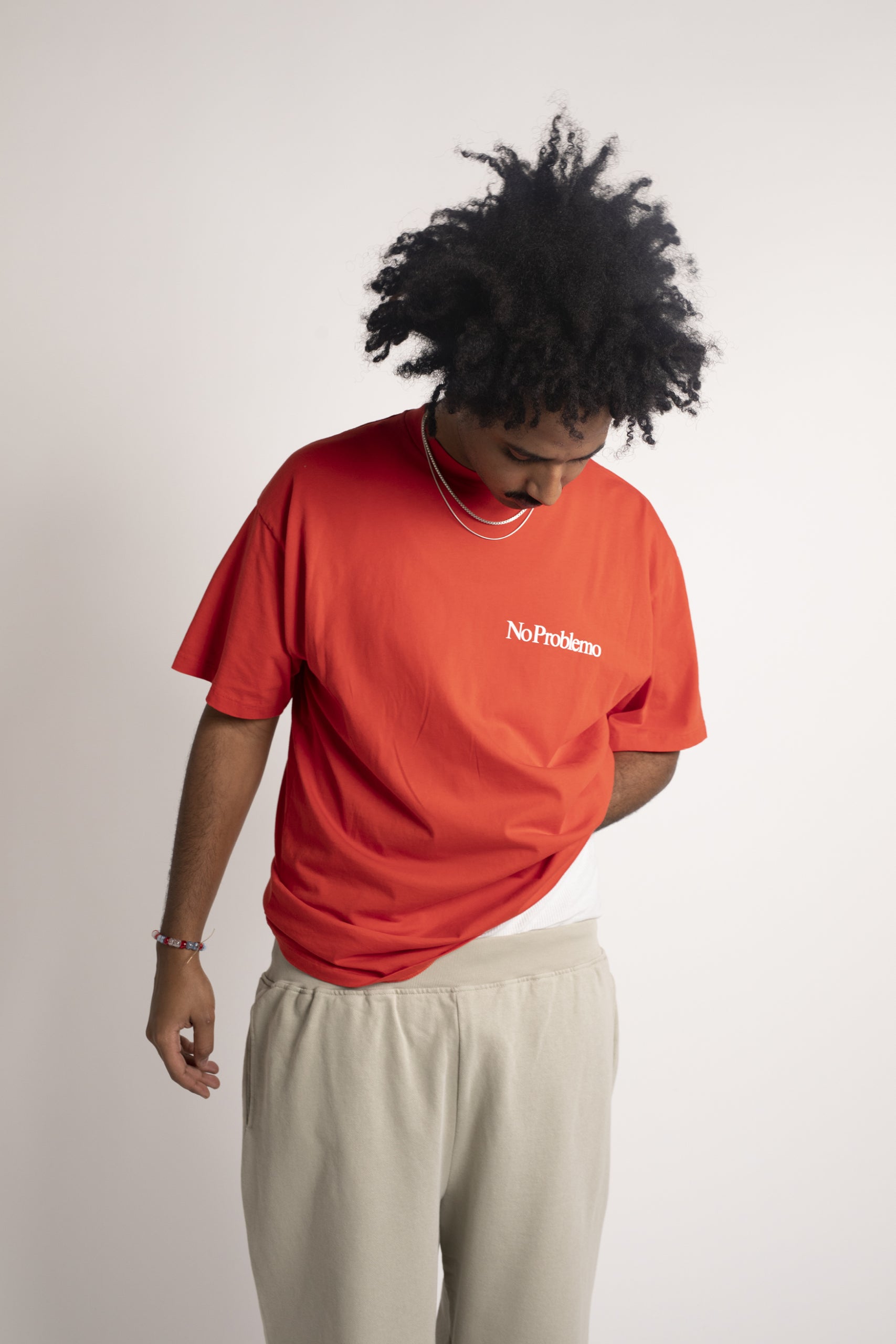 Man with hair wearing aries mini problemo tee in red with silver chains and tan sweatpants