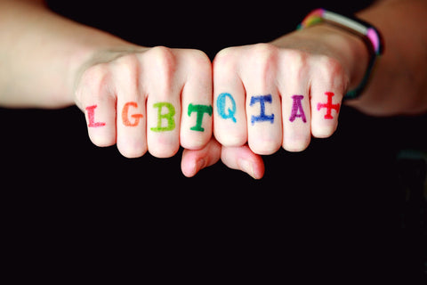 The acronym LGBTQIA+ written in rainbow colors on the knuckles of a person