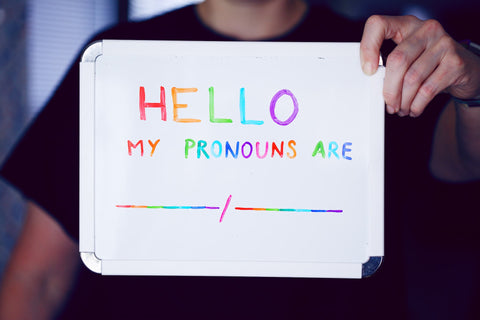 Person holding a sign that says "Hello My Pronouns Are" in rainbow colors
