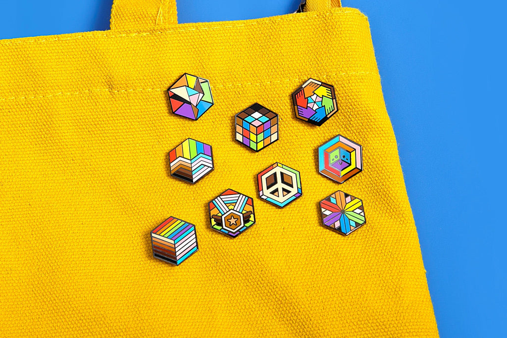 9 pride enamel pins on a yellow canvas tote bag with blue background