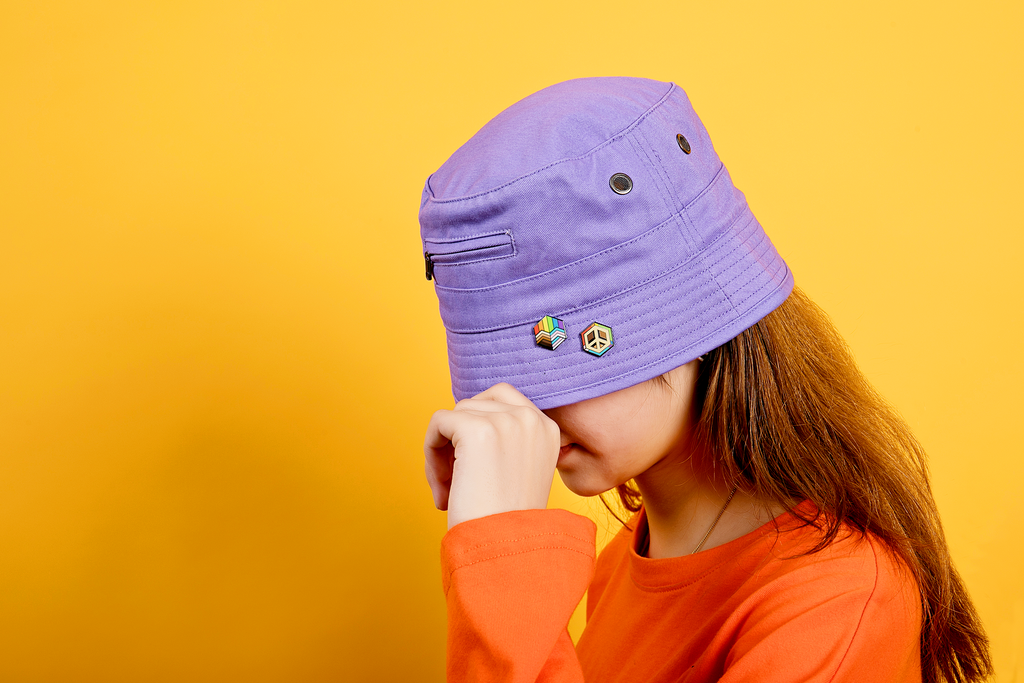 girl with 2 proud cubes pride pins on purple bucket hat with orange background