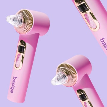 Three pink facial massage tools on a purple background.