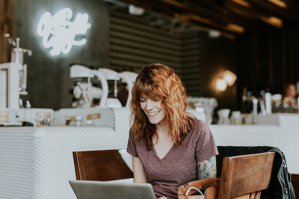 Photo by Brooke Cagle. Woman with red hair sitting at a table in a coffee shop smiling and on her laptop