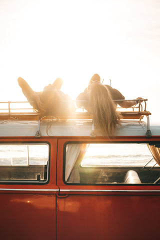 Red van with two women laying on top bathing in the sun. Photo by ROMAN ODINTSOV