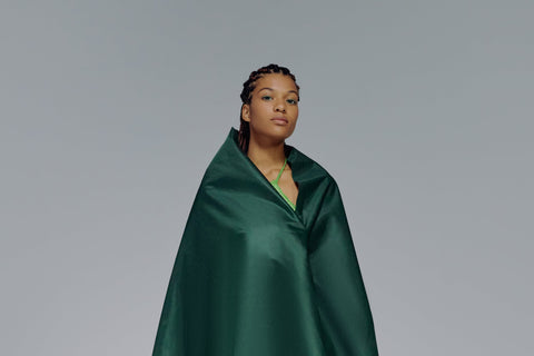 Black woman with braids looking confident wrapped in a green cape. Photo by Ron Lach