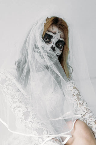 Kobieta w strasznym makijażu pozuje do zdjęcia w białej sukni i welonie