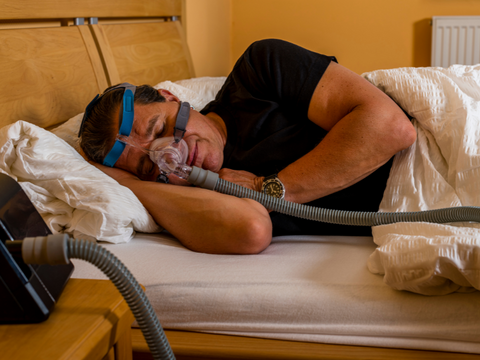 Man sleeping in bed while wearing sleep apnea mask and cpap