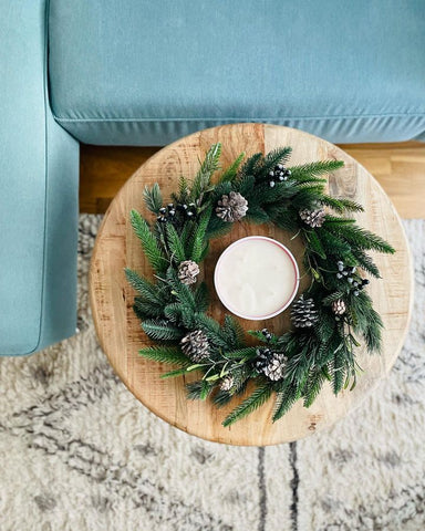 A holiday wreath sitting on a living room table beside a blue couch with a big candle in the middle