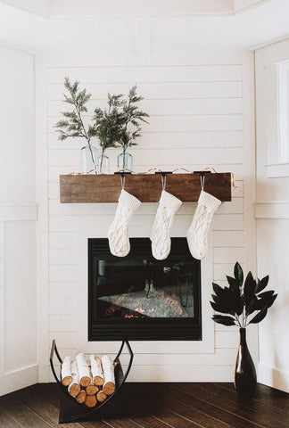 Minimalist holiday decor, three stockings hanging over a mantle with a pile of wood and plant beside it