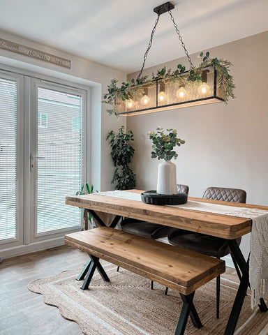 An overhead light hangs above a kitchen table, decorated with greenery, a big plant as the centrepiece