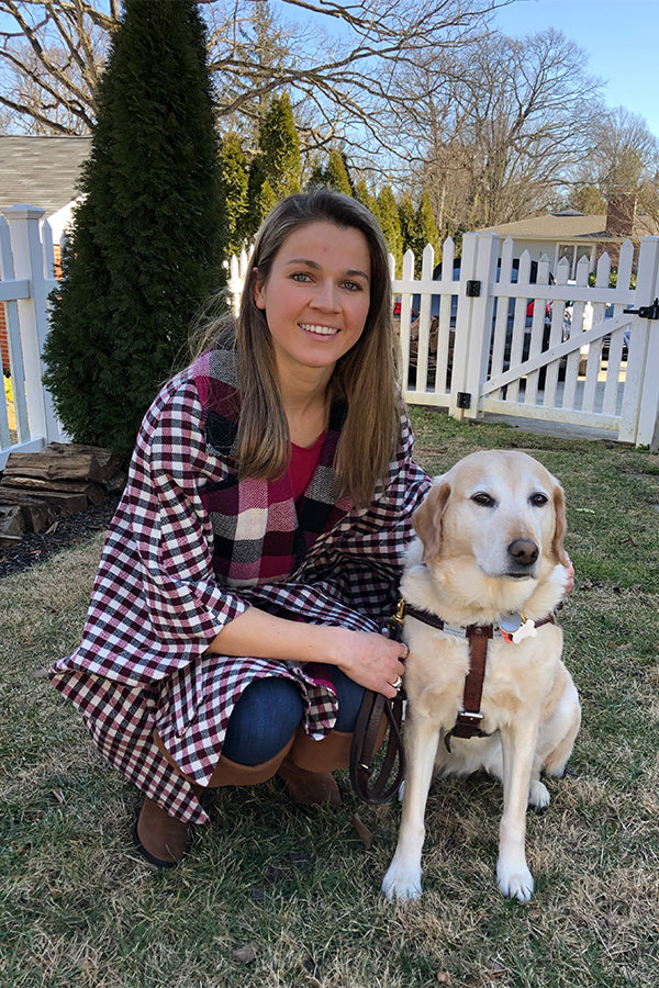 Becca crouches next to her Seeing Eye Dog Birdie - both are seen smiling towards the camera