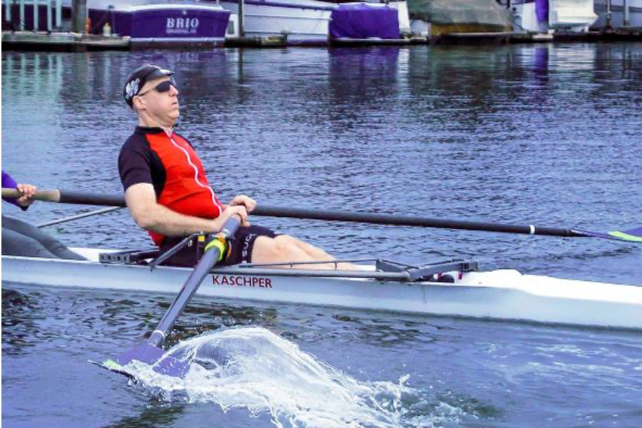 Chris rowing stroke in a red and black jersey, black sports shades and cap. 