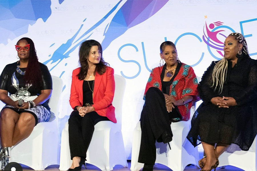 Sharon speaking at Success Women's Conference. A panel of four ladies, Sharon sits second from the left, wearing a red blazer and black pants.