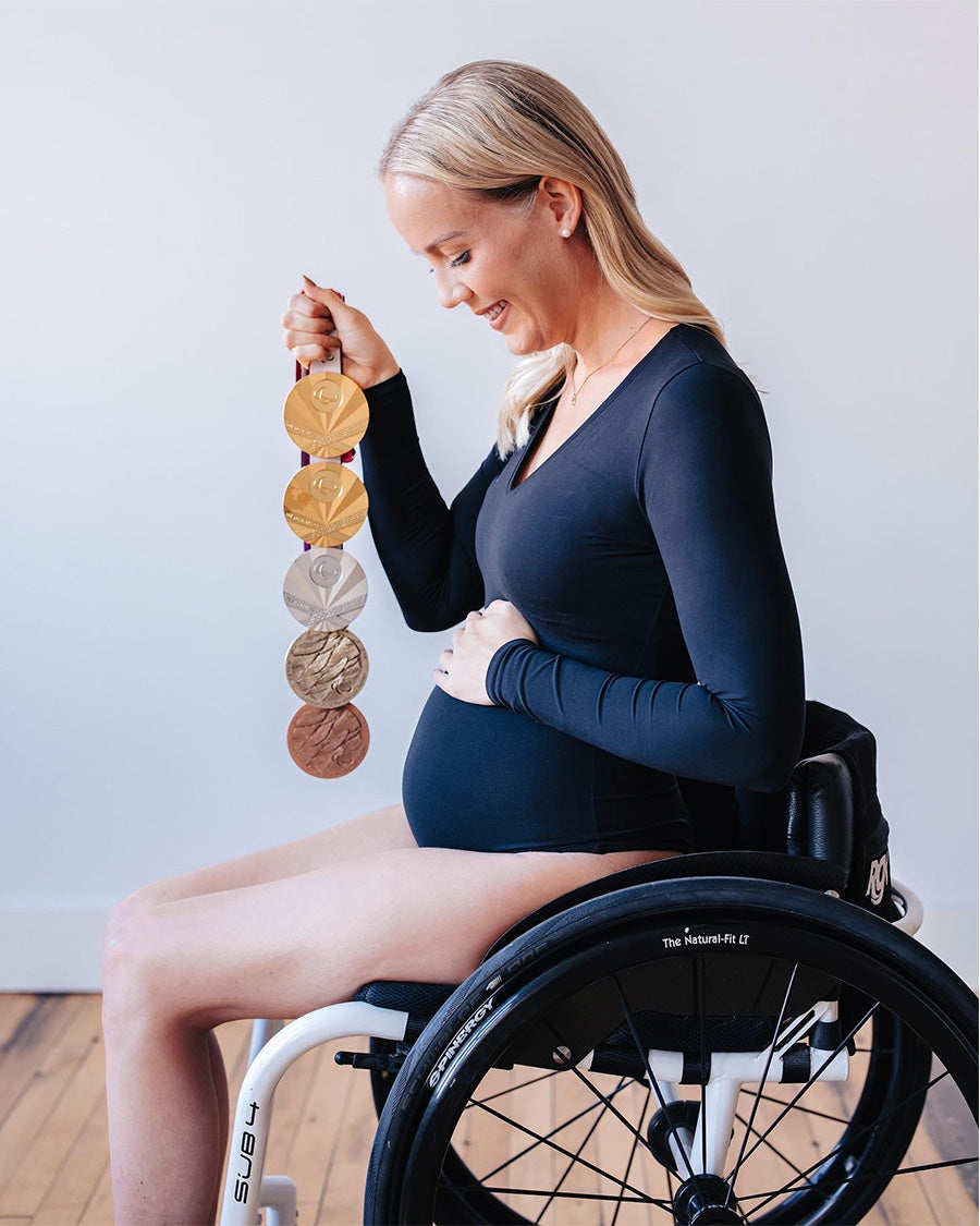 Side on, Mallory smiles, looking down at her baby bump. In her right hand, she holds her five Olympic medals.