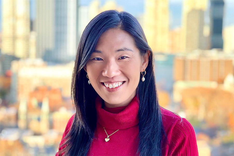 An image of Ming, she's wearing a red turtleneck sweater with the city skyline on the background.