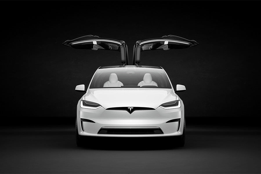 Photographed head on, the Tesla model X in white, with its wing doors open, set against an infinite black backdrop.