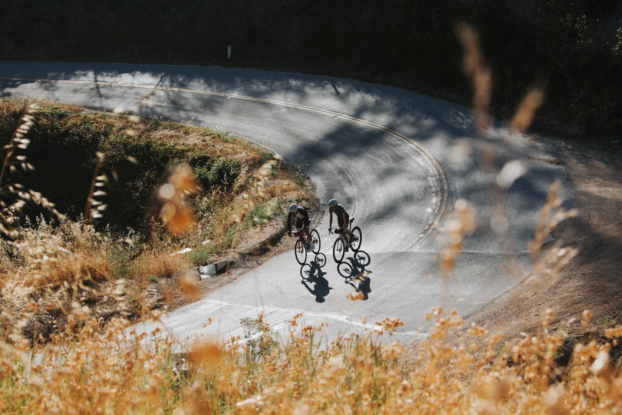 2 cyclists enjoying a road ride on a country mountain road, riding bikes with ALMSTHRE cycling bags on the Handlebars and under the saddle.