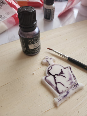 White icing gravestone with purple edible pain detailing on a chopping board