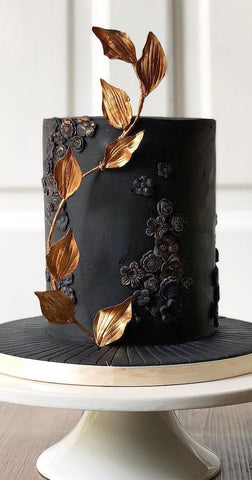 Black iced cake with black flower detailing around the side and striking gold leave design.