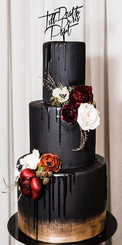 Black iced wedding cake with rose gold painted edge around the bottom. White, orange and dark red flowers and topper saying "till death do us part".