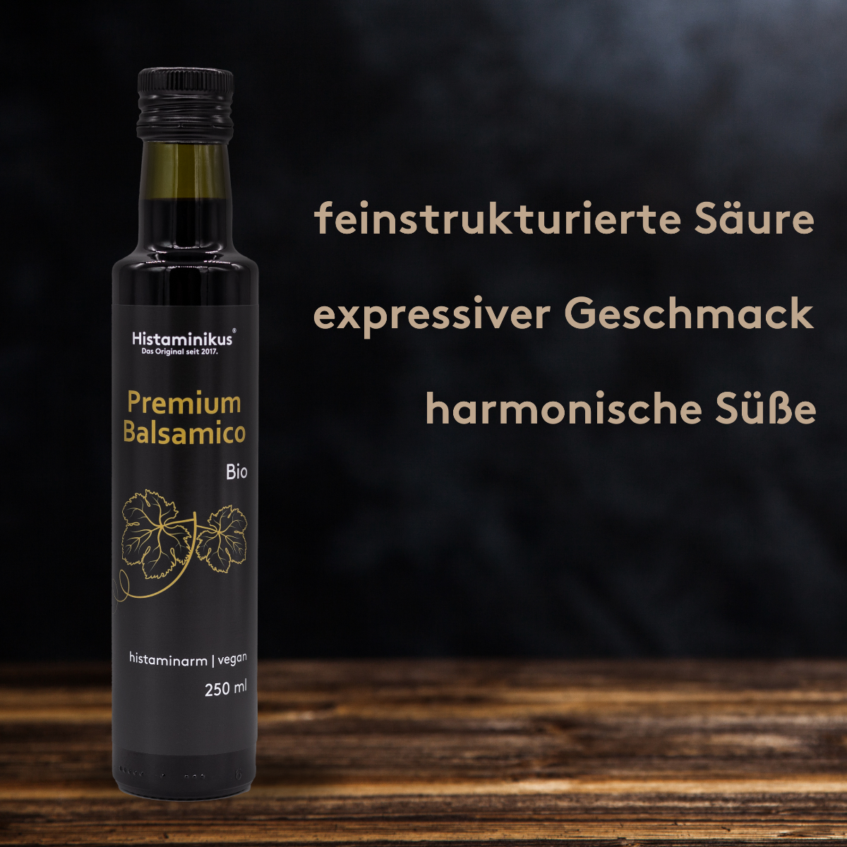 Die Grafik zeigt die Flasche mit dem Premium Balsamico und rechts neben der Flasche sind drei positive Eigenschaften des Balsamico aufgeführt: feinstrukturierte Säure, expressiver Geschmack, harmonische Süße. Der Hintergrund ist dunkel gehalten und die Flasche steht auf einem dunkelbraunen Holztisch.