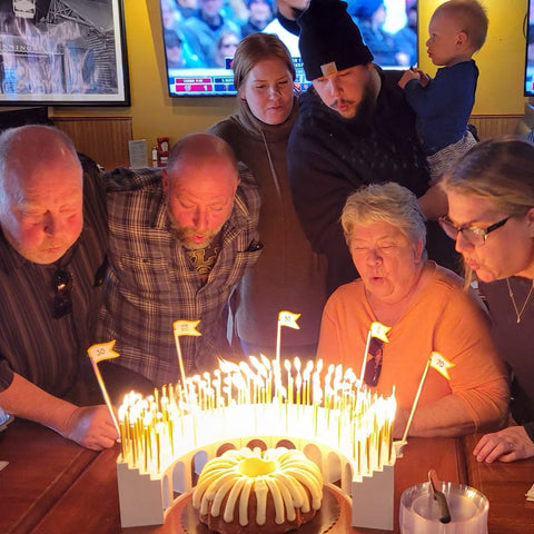 Multi-generational family celebrating a 60th birthday with a Nothing Bundt Cake surrounded by a Celebration Stadium with 60 lit birthday candles/