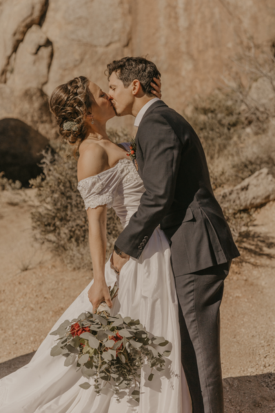 A bride and groom kiss, while holder the bridal bouquet in Arizona