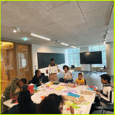 Space black studios running a STEM workshop (children are sat around a table designing their own houses with pens/paper/card). 