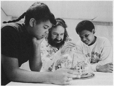 Photo of Seymour Papert and two children, testing his LOGO turtle robot. 