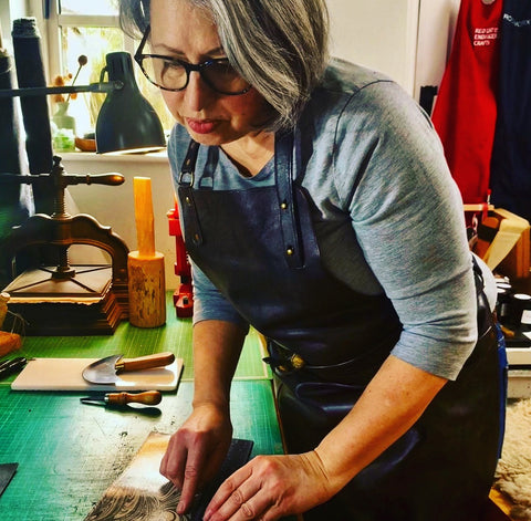 ROCWORX Rachel O'Connell working on marbled leather in her studio.  Tools are on the bench and the artist is wearing a leather apron