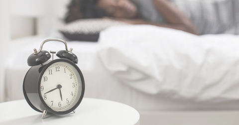 Image shows a woman sleeping behind an alarm clock. Sleep gifts at Tangled Roots