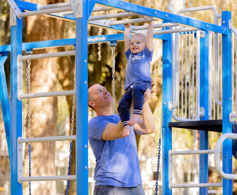 Dad helping toddler across SwingSesh monkey bars