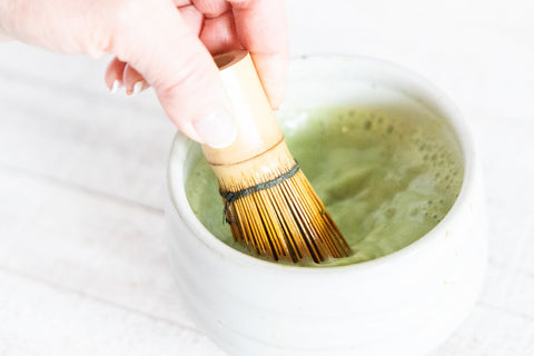 whisking matcha with traditional bamboo whisk in bowl 