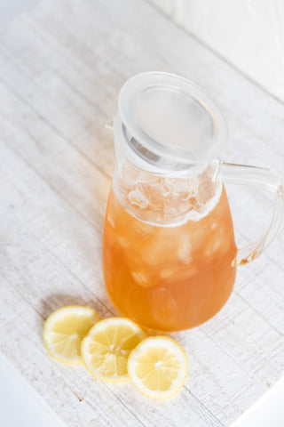 Ice cubes and tea in a pitcher with lemon slices beside