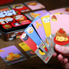 Close up of a hand holding Sushi Go cards. The game tin is in the background.