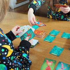 A child in the foreground holding a hand of Sleeping Queens cards facing towards us. Cards are laid out on the table in front of them.