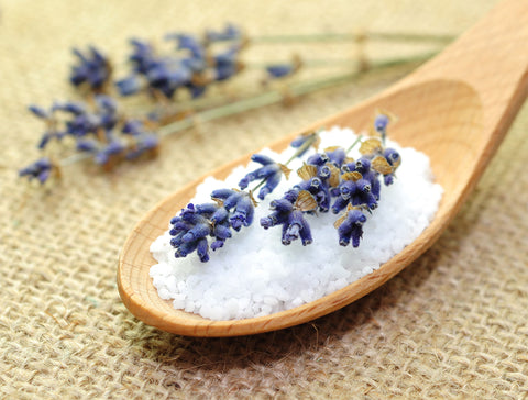 wooden spoon with salt and topped with lavender flowers with additional flowers placed as decorations