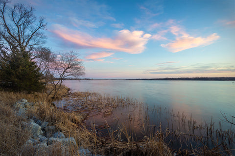 view of large body of water from a rocky shoreline with blue skies and a few clouds after the sun has set