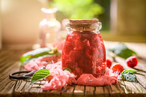 Raspberries in glass jar on table in foreground with raspberry leave in the background