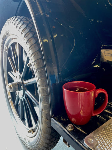 A red mug of tea on a step below the car door