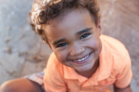 A small boy with curly hair and a big smile, wearing an orange t-shirt