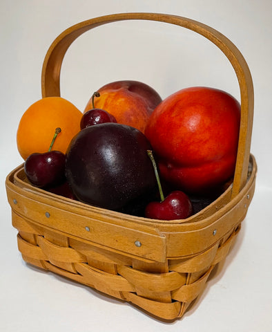 A basket filled with stone fruits: a nectarine, a peach, an apricot, a plum, and several cherries.